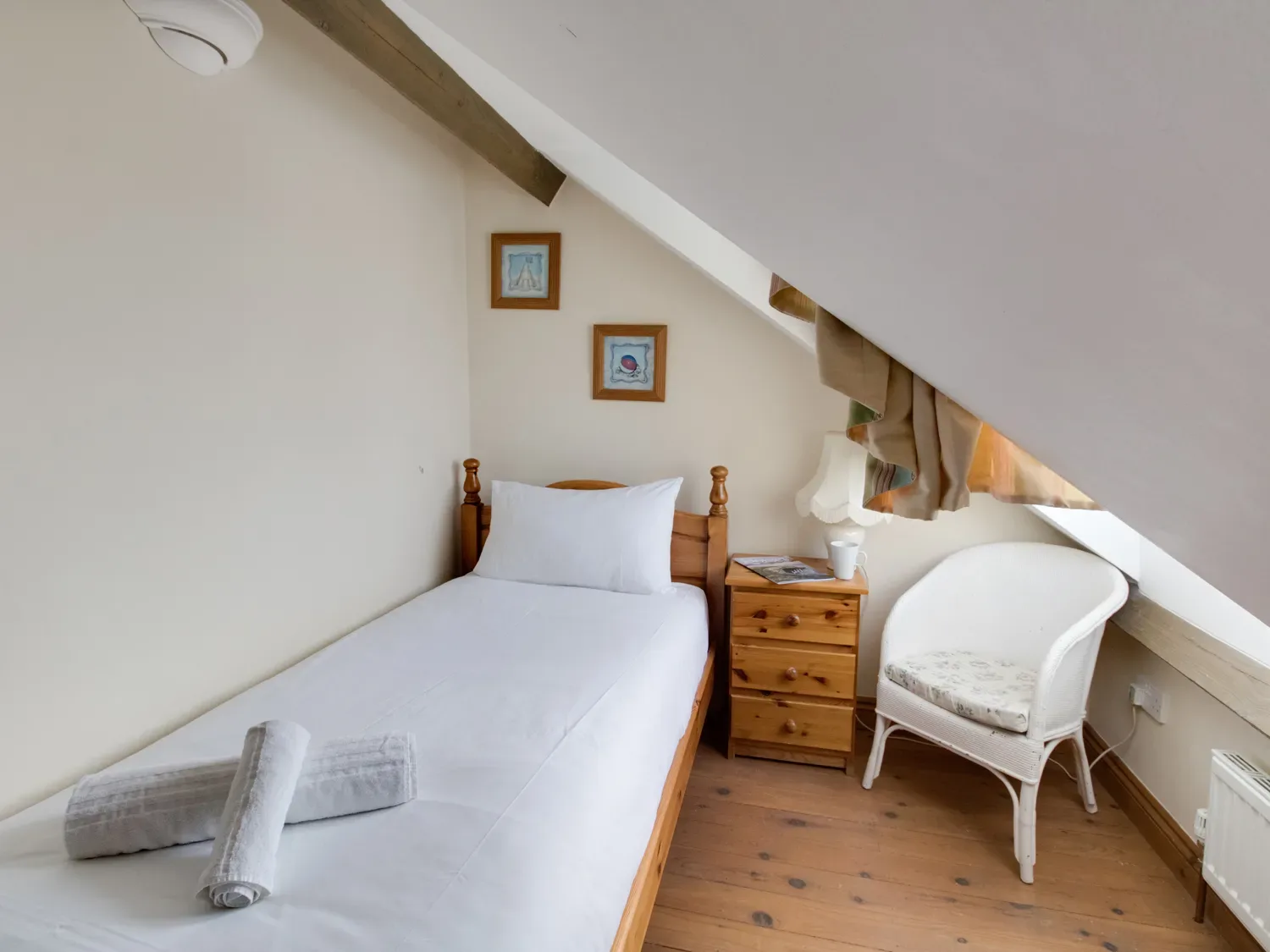 A compact bedroom with a single bed, white bedding, and a bedside table beneath a sloped ceiling.