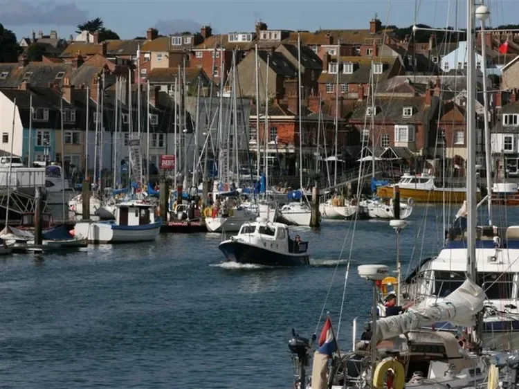 A harbor filled with sailboats and motorboats, with buildings along the waterfront.
