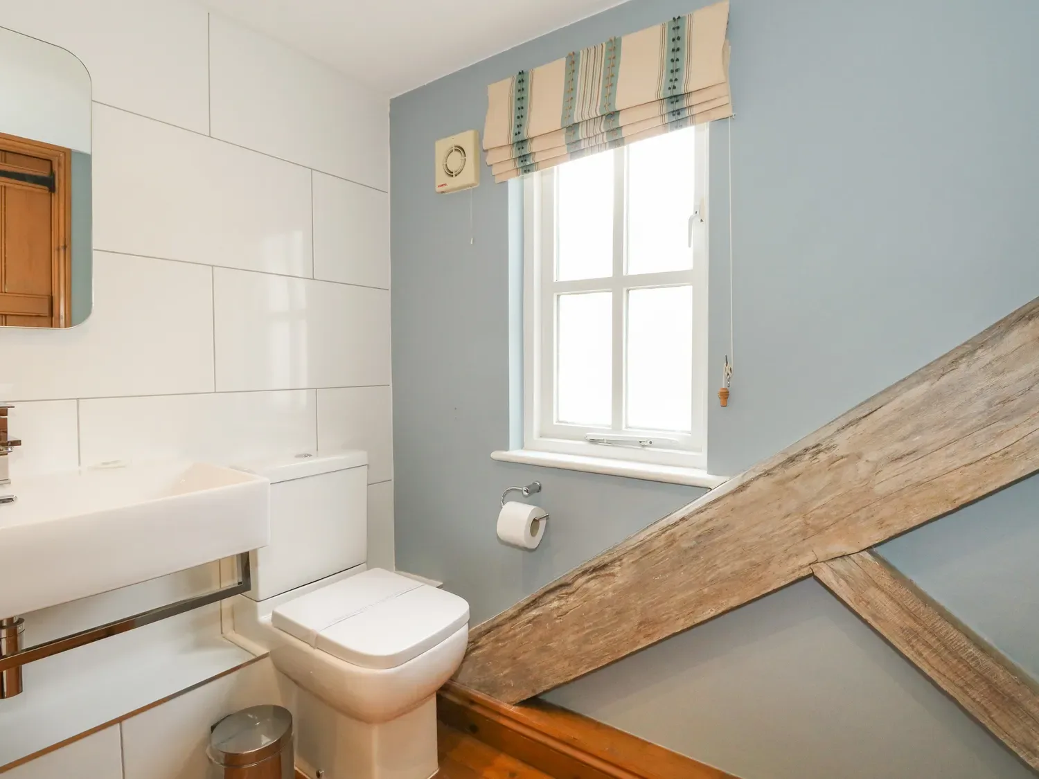 A bathroom with a toilet, sink, mirror, and window.