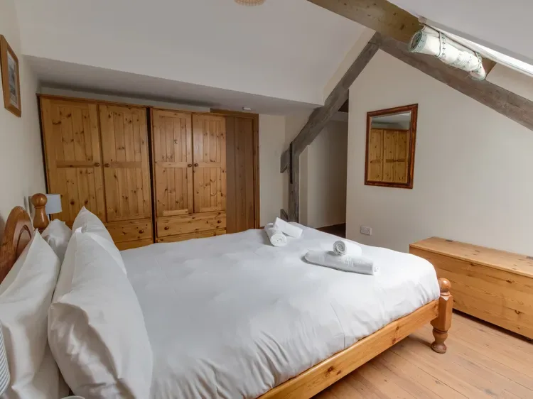 A bedroom with a wooden bed and white bedding beneath a sloped ceiling.