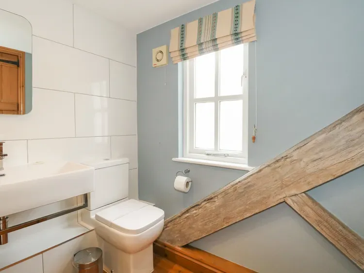 A bathroom with a toilet, sink, and a window beneath a striped shade.