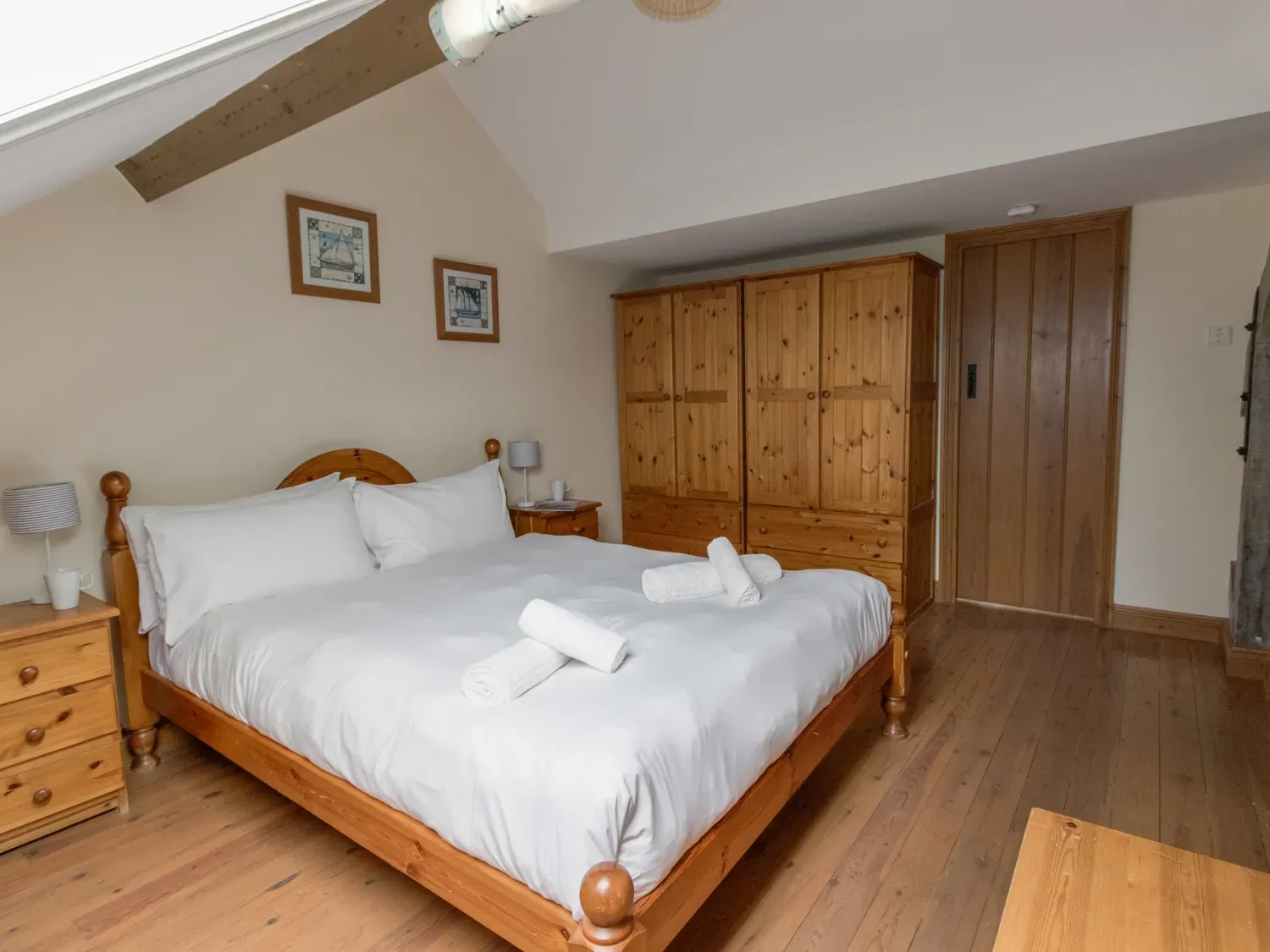 A bedroom with a wooden bed, white bedding, bedside tables, and wardrobes.