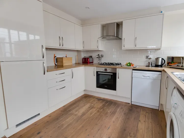 A bright kitchen with white cabinets, countertops, and wood flooring.