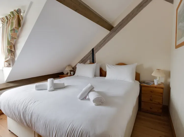 A bedroom with a neatly made bed and towels beneath exposed ceiling beams.