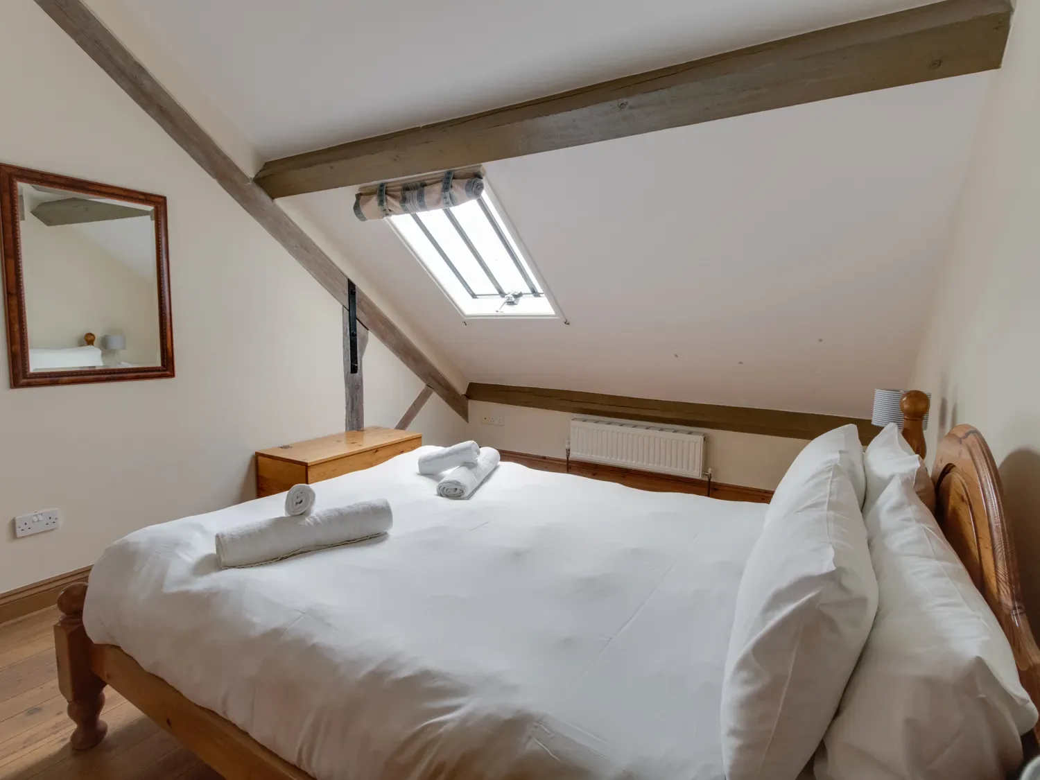 A bedroom with a wooden bed frame white bedding towels on the bed wooden chest a wall mirror and a skylight window at Georges House Brewers Quay Harbour