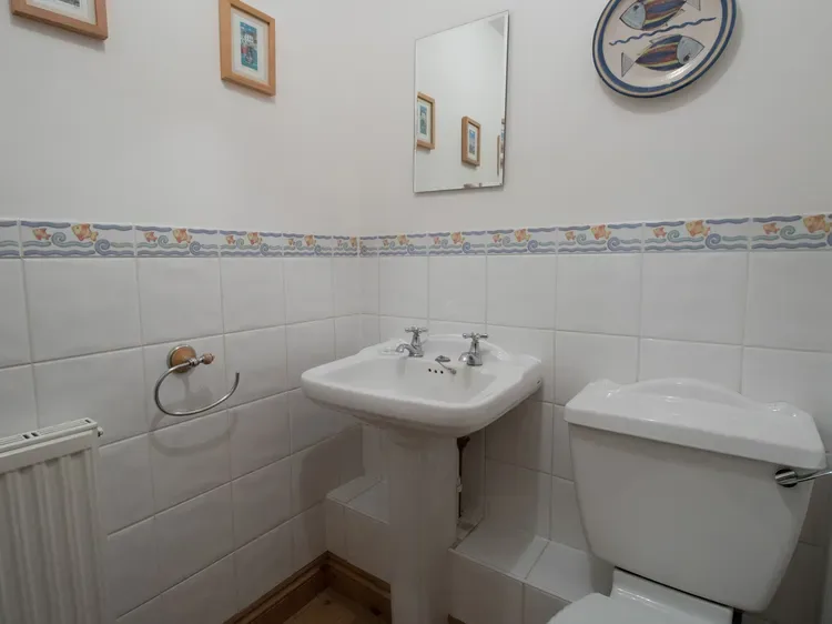 A tiled bathroom with a pedestal sink, mirror, and toilet.