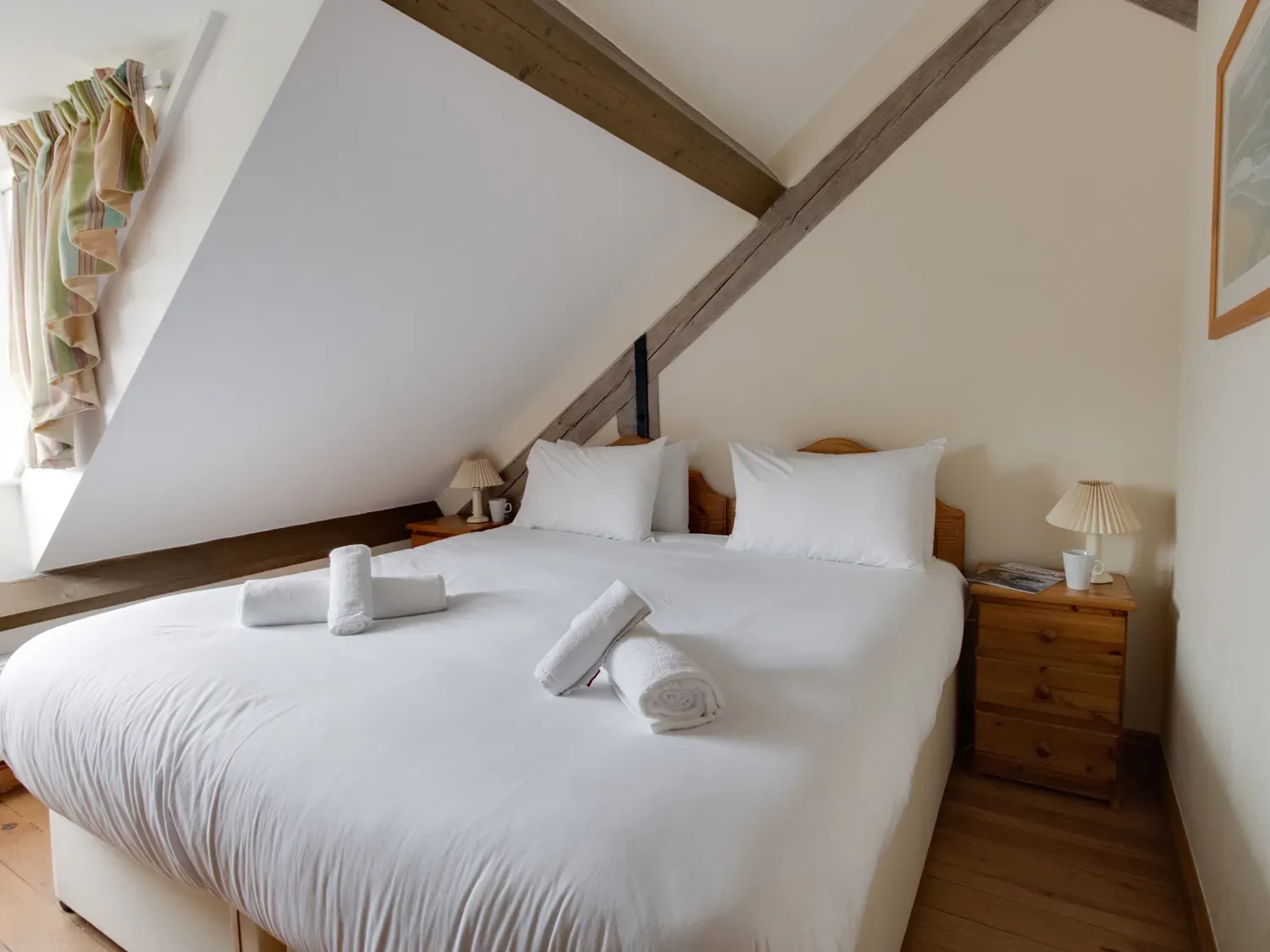 A bedroom with a double bed rolled towels bedside tables lamps and a window with curtains at Georges House in Brewers Quay Harbour