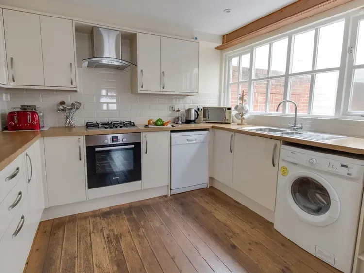 A bright kitchen with white cabinets, wood flooring, and a large window.