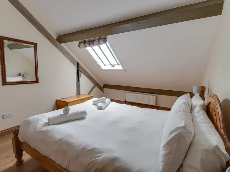 A bright bedroom with a large bed beneath a sloped ceiling and skylight.
