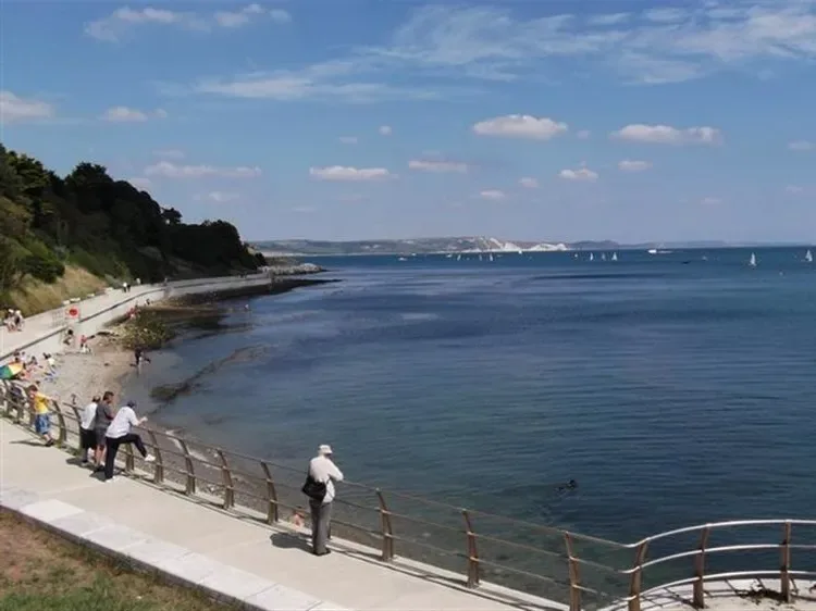 A waterfront promenade overlooks a broad bay with boats in the distance.