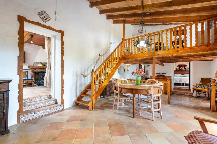 Interior rústico con una escalera de madera, barandilla elevada y mesa de comedor.