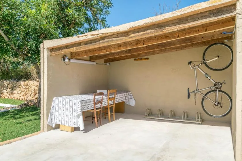 Un espacio exterior cubierto tiene una mesa con sillas y una bicicleta montada en la pared.