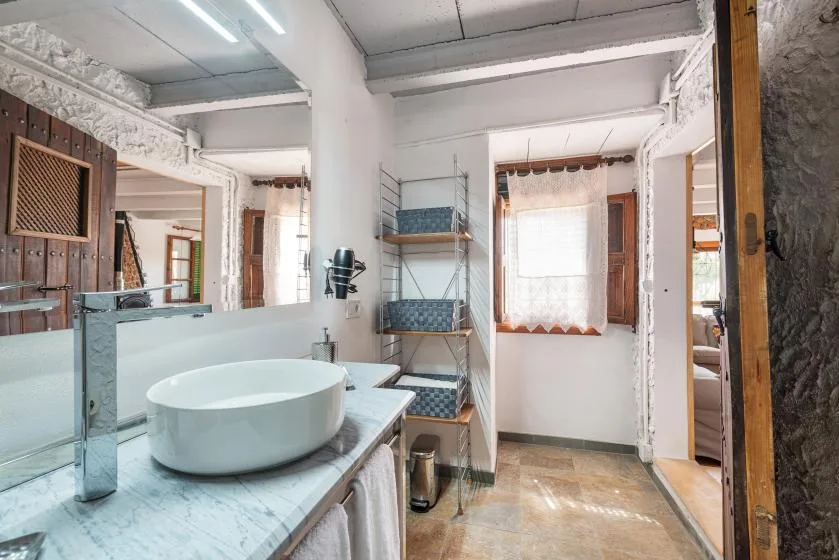 Un baño con un lavabo blanco sobre la encimera y una ventana con cortina translúcida.