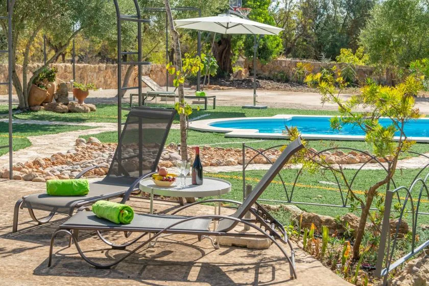 Zona de piscina al aire libre con asientos reclinables y una mesa a la sombra.