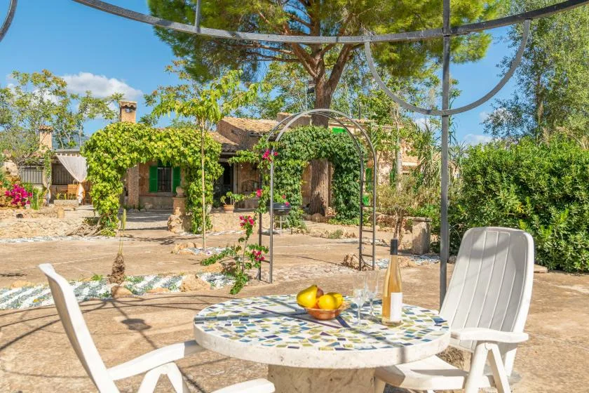 Un patio soleado con una mesa de mosaico y enredaderas junto a una casa de piedra.