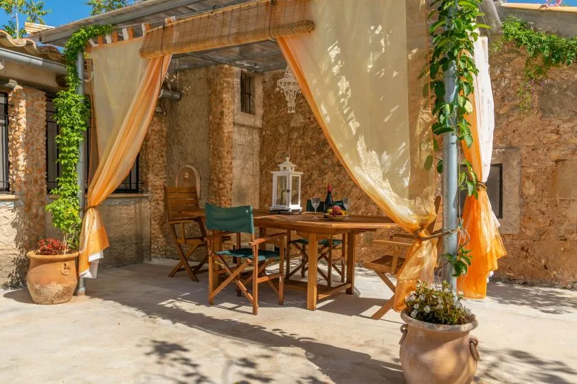 Comedor en un patio de piedra con una mesa de madera bajo toldos de tela.