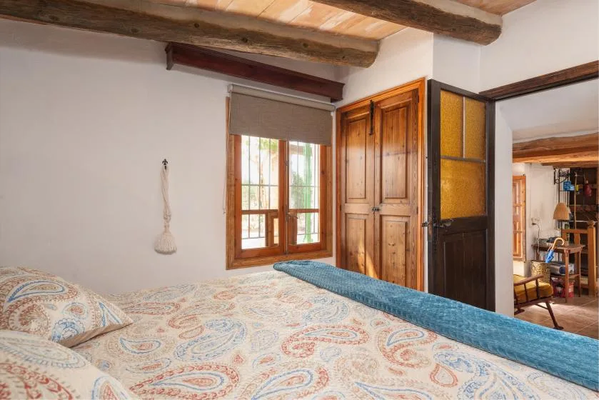 Un dormitorio con una colcha estampada, un armario de madera y una ventana.