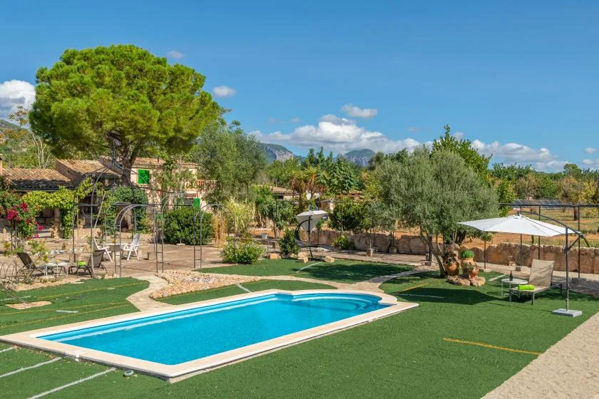 Una piscina al aire libre está junto a un jardín con árboles y asientos.