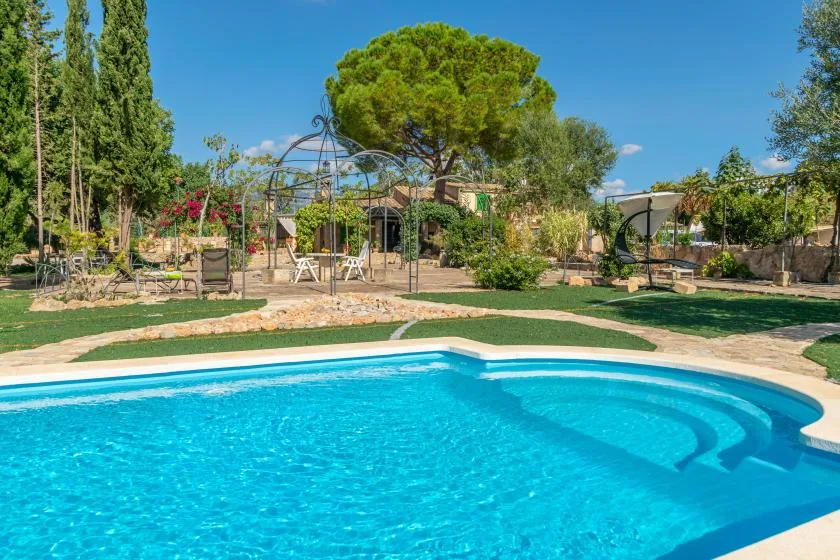 Una piscina al aire libre junto a un jardín con árboles y asientos.