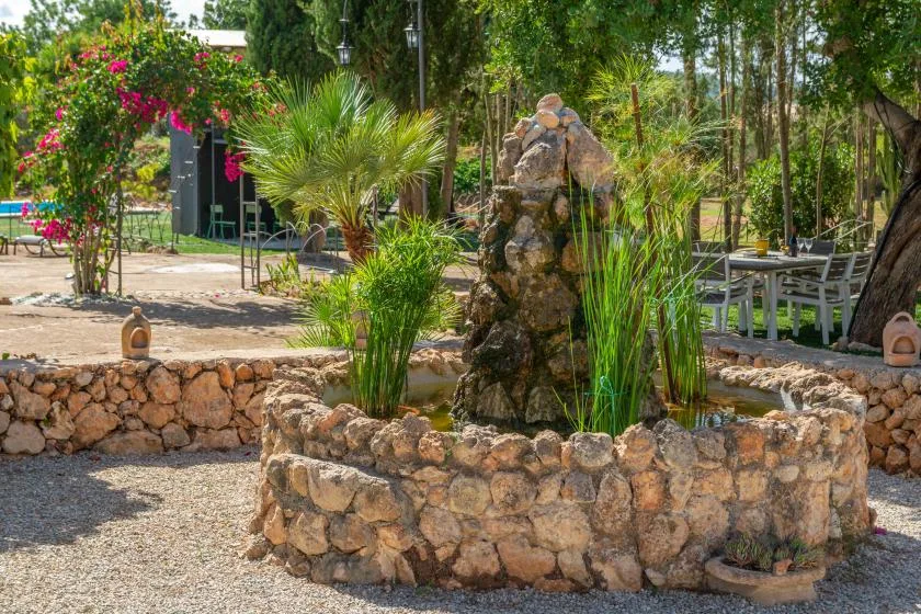 Un jardín ajardinado con una fuente de piedra rodeada de plantas y asientos al aire libre.