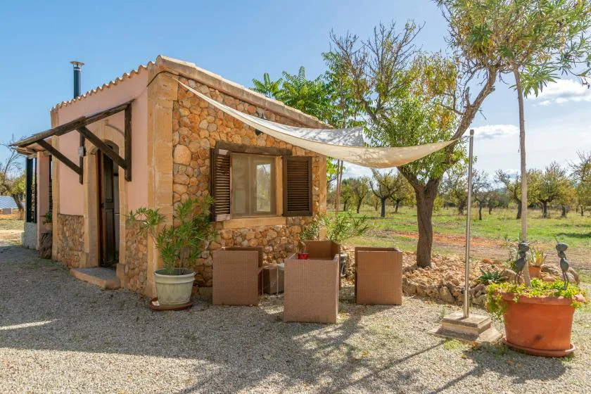 Una pequeña casa de piedra con una zona de estar al aire libre a la sombra en un jardín.