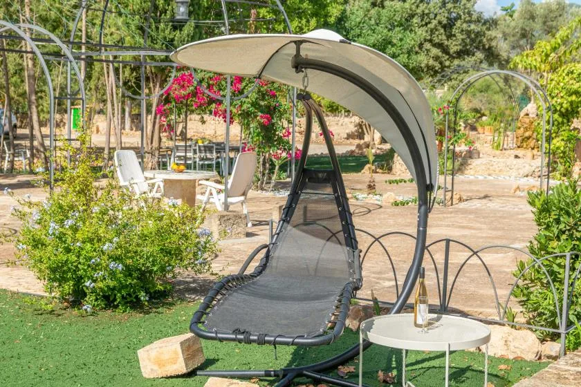 Una zona de descanso al aire libre con una silla colgante sombreada y vegetación alrededor.