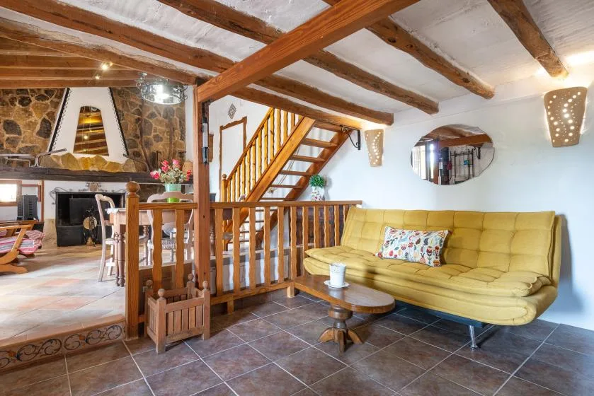 Una sala rústica con un sofá amarillo y una escalera de madera.