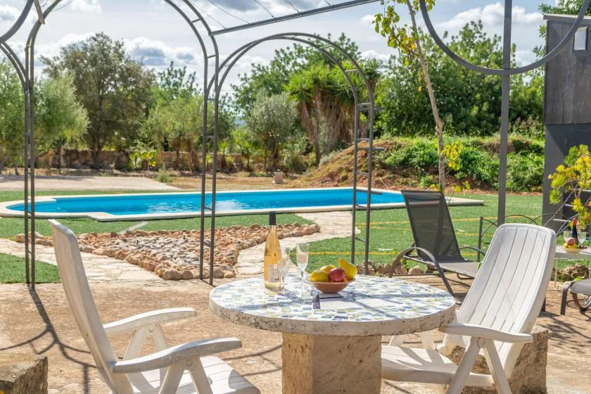 Una zona de estar en el patio junto a una piscina, con una mesa bajo una pérgola metálica.