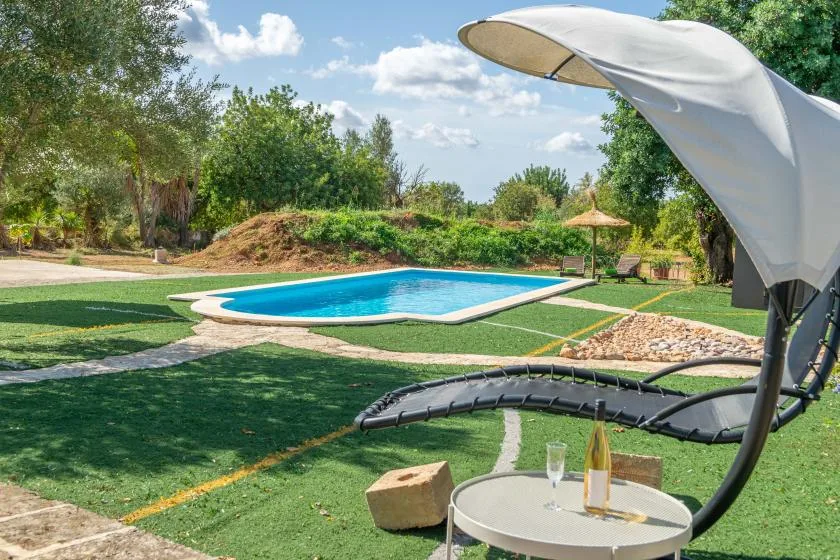 Una piscina al aire libre está junto a un césped y una zona de descanso sombreada.
