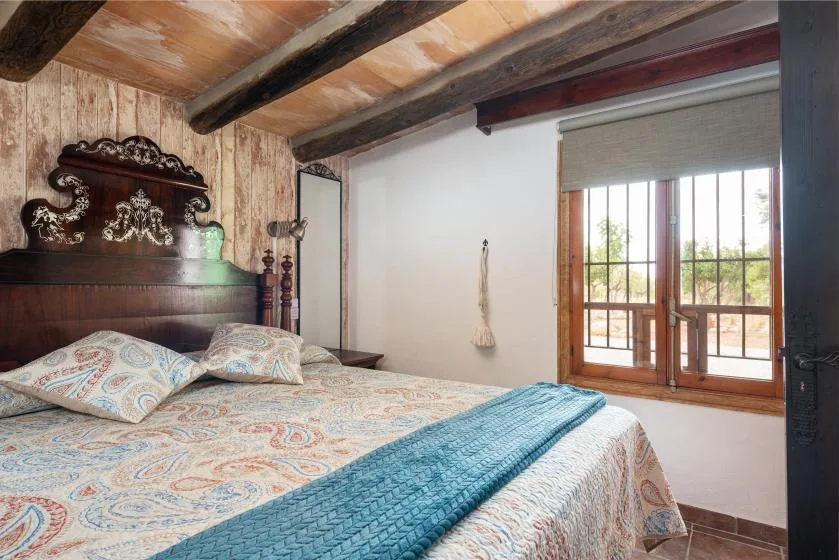 Un dormitorio con ropa de cama estampada y puertas de madera que dan a un balcón.