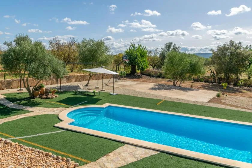 Una piscina al aire libre está junto a un jardín con césped y una zona de descanso con sombra.