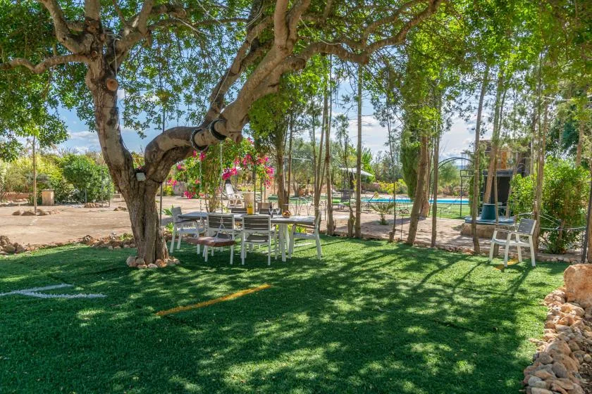 Una zona de estar sombreada en un jardín bajo un árbol grande, con una piscina cerca.