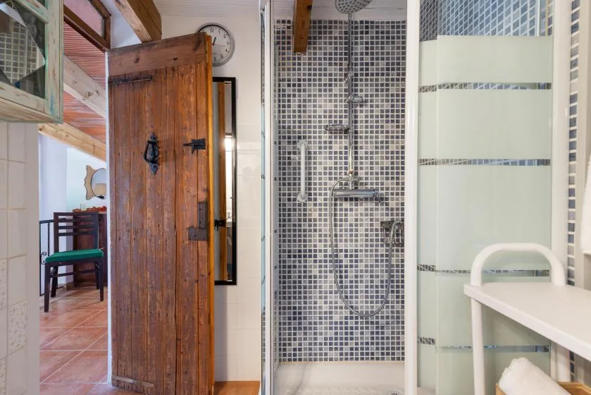 Un baño alicatado con una ducha de vidrio y una puerta de madera abierta.