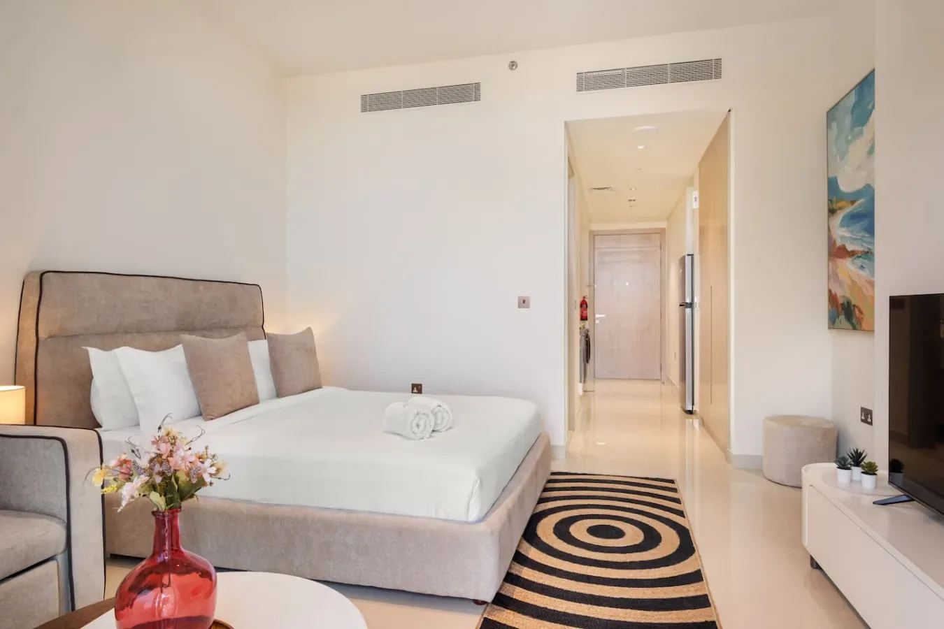 Un dormitorio luminoso con una cama bien tendida y una alfombra estampada.