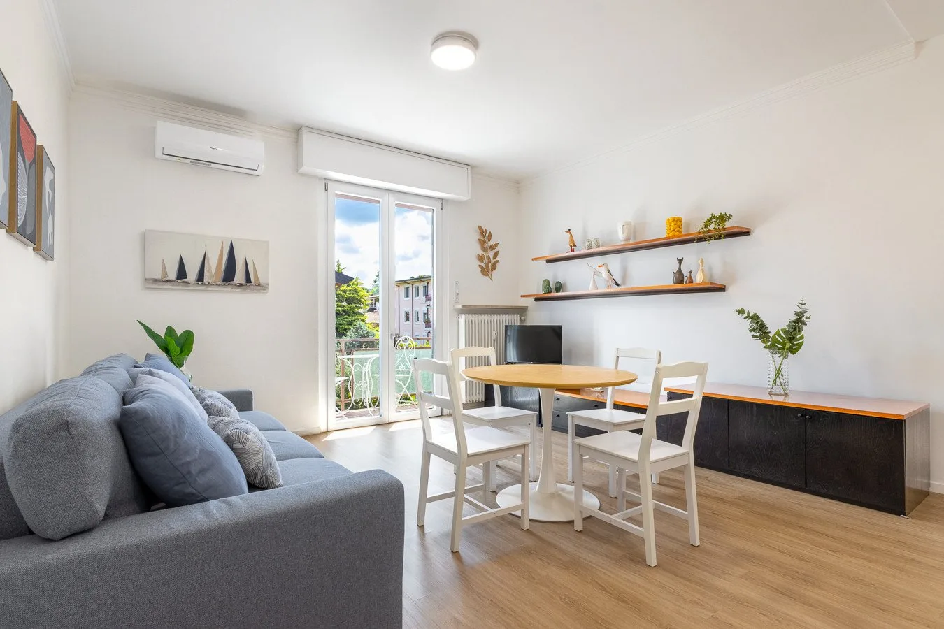 Una luminosa sala-comedor tiene un sofá, una mesa de comedor y puertas al balcón.