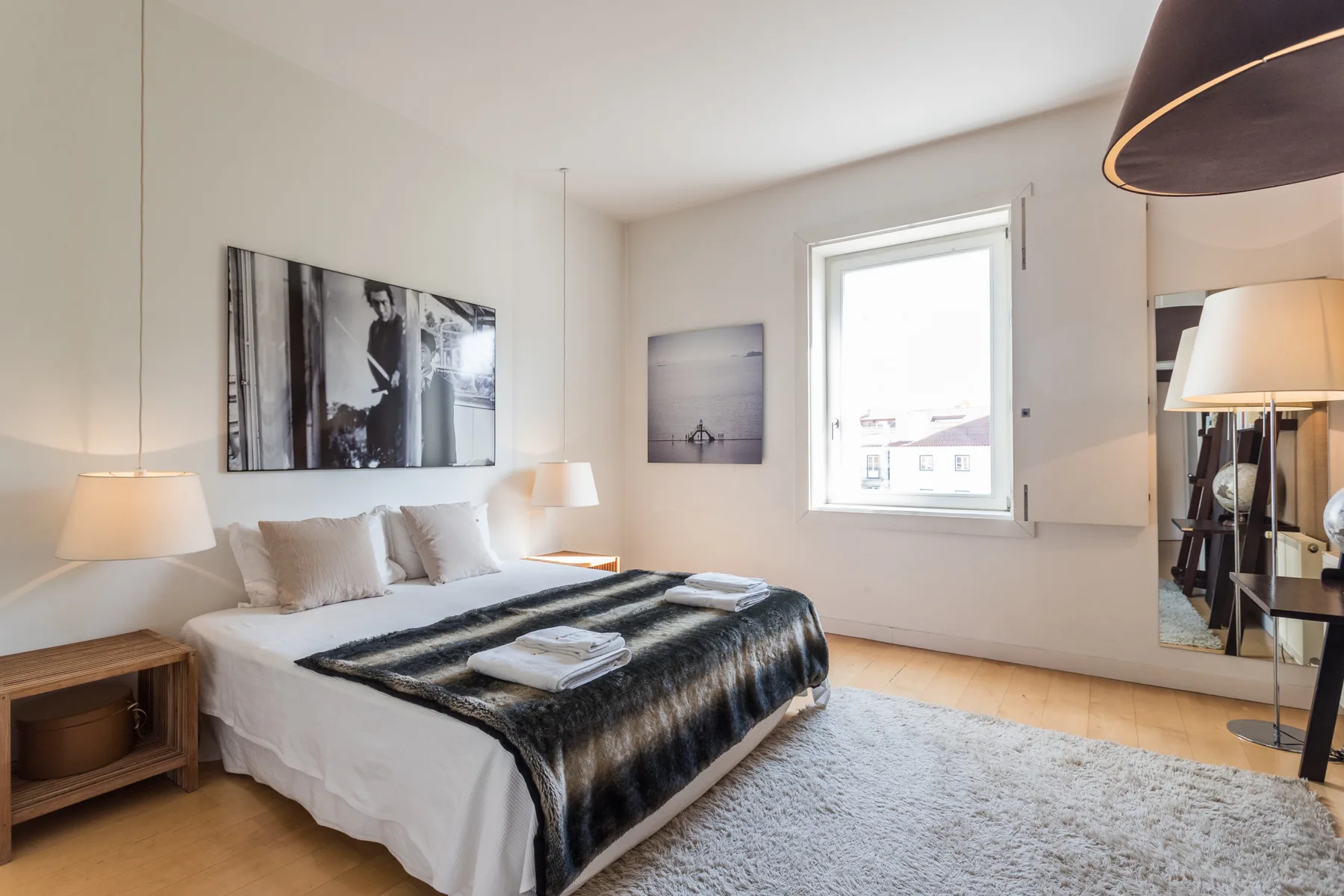A bright bedroom with a double bed, bedside tables, and a window.