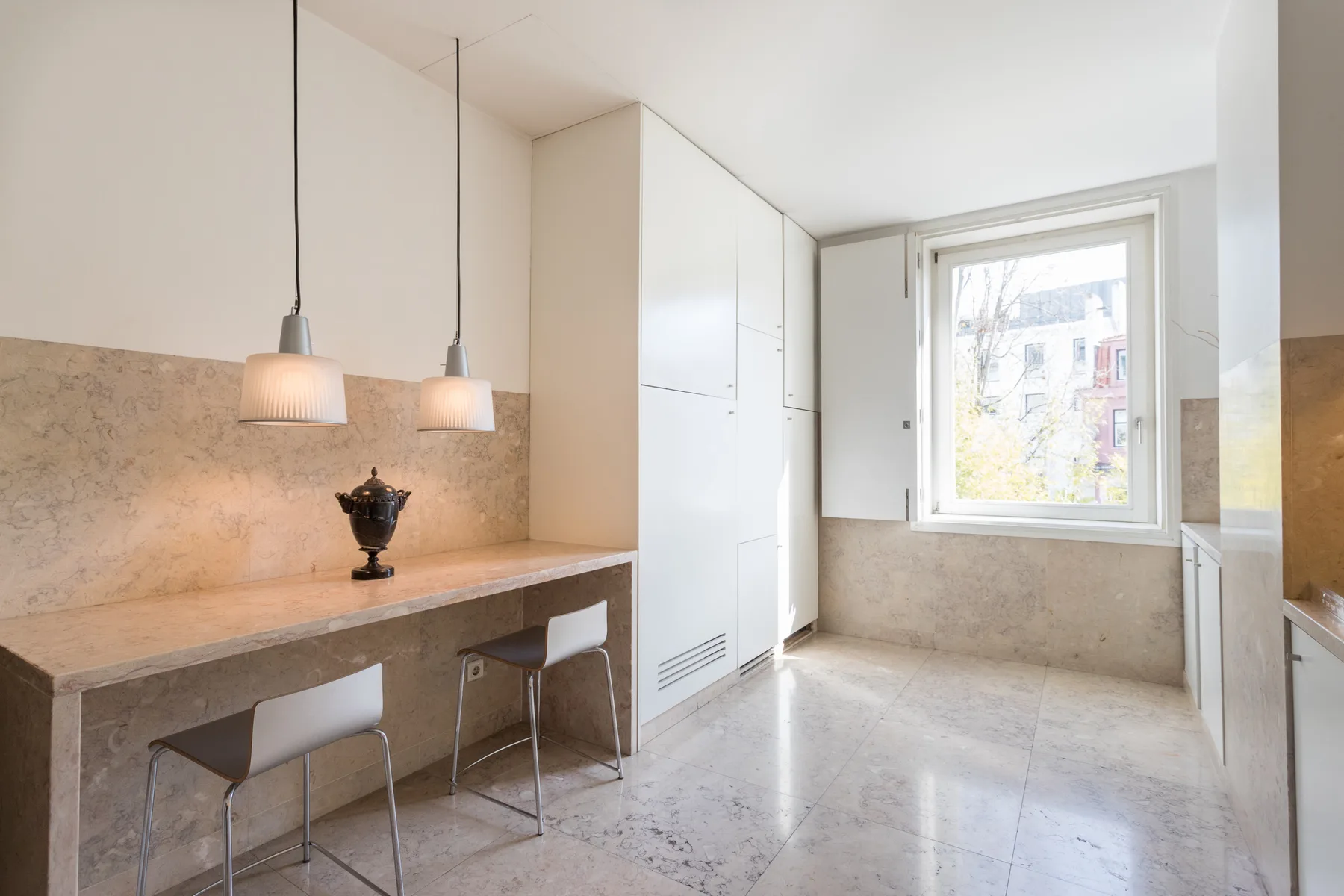 Bright kitchen with a long counter, pendant lights, and a large window.