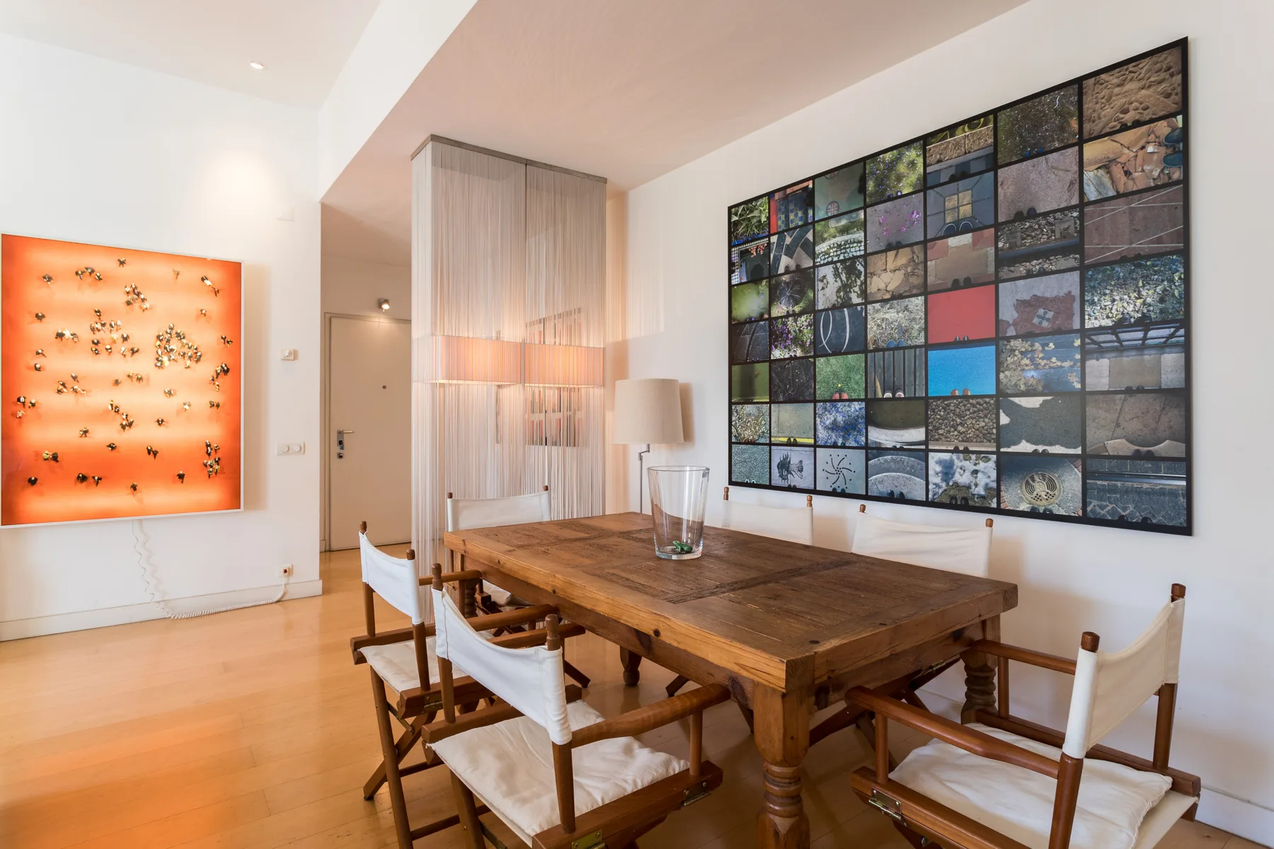 A dining area with a wooden table, chairs, and a large wall display of photographs.