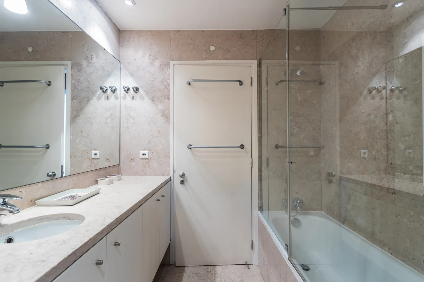A bathroom with a long vanity and a glass-enclosed bathtub.
