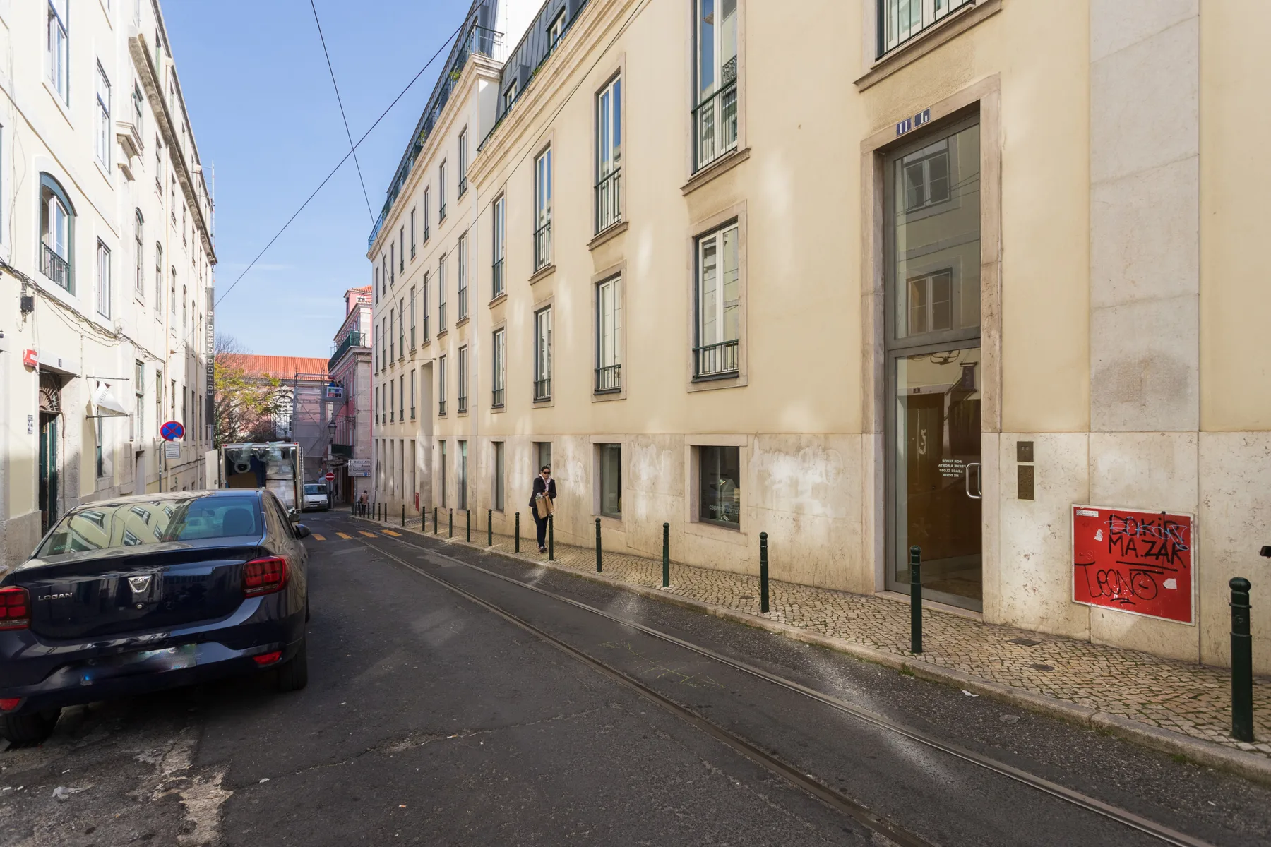 A narrow city street lined with tall buildings and parked cars.