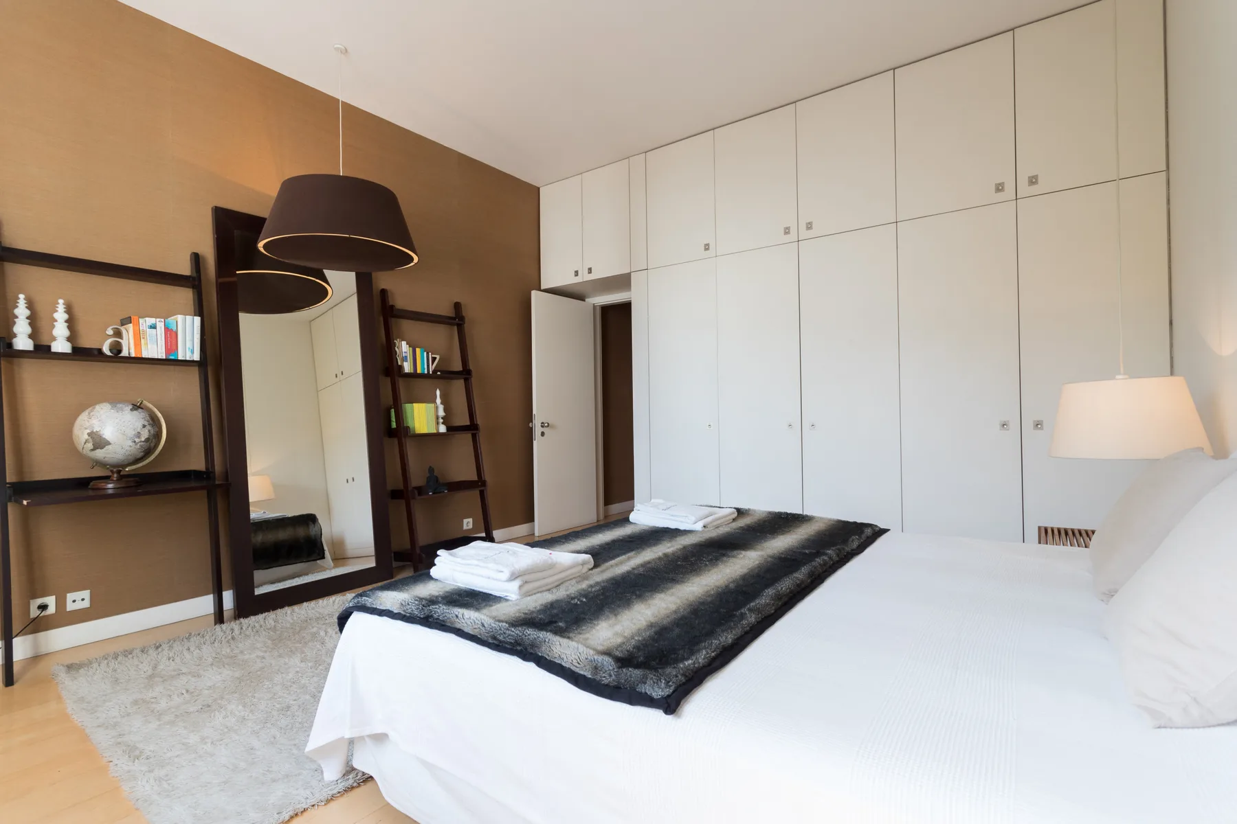 A bedroom with a bed, folded towels, and built-in cabinets.
