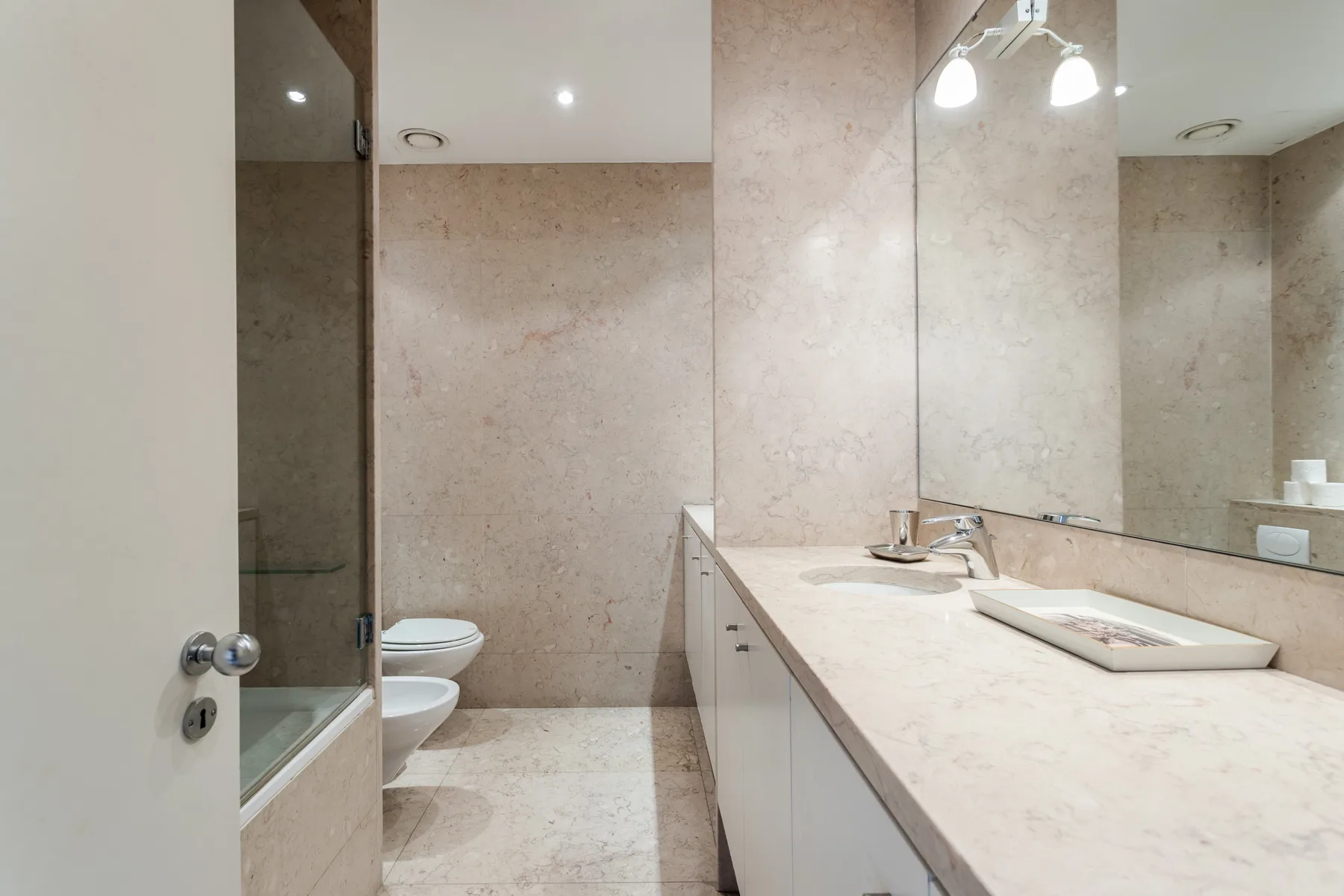 A bathroom with a long vanity, sink, and large mirror.