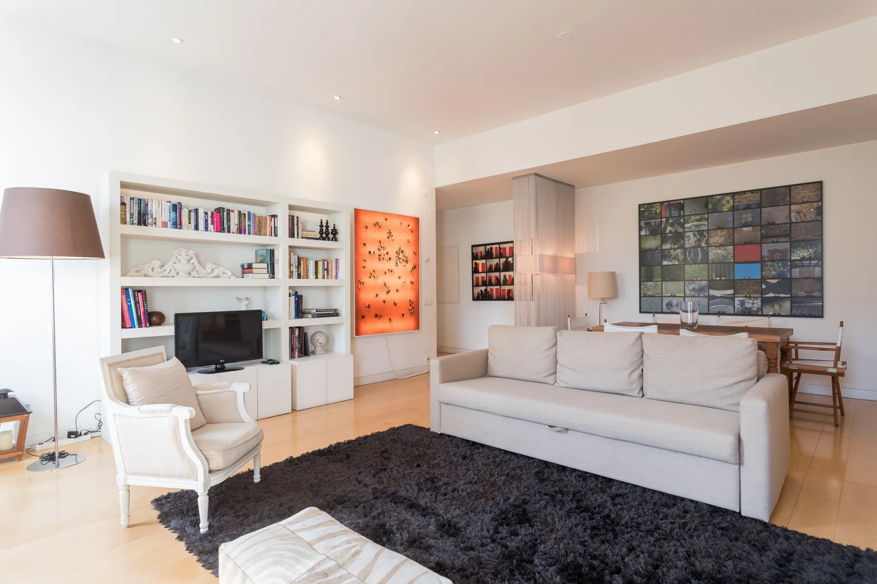 A bright living room with seating arranged around a dark rug and television.