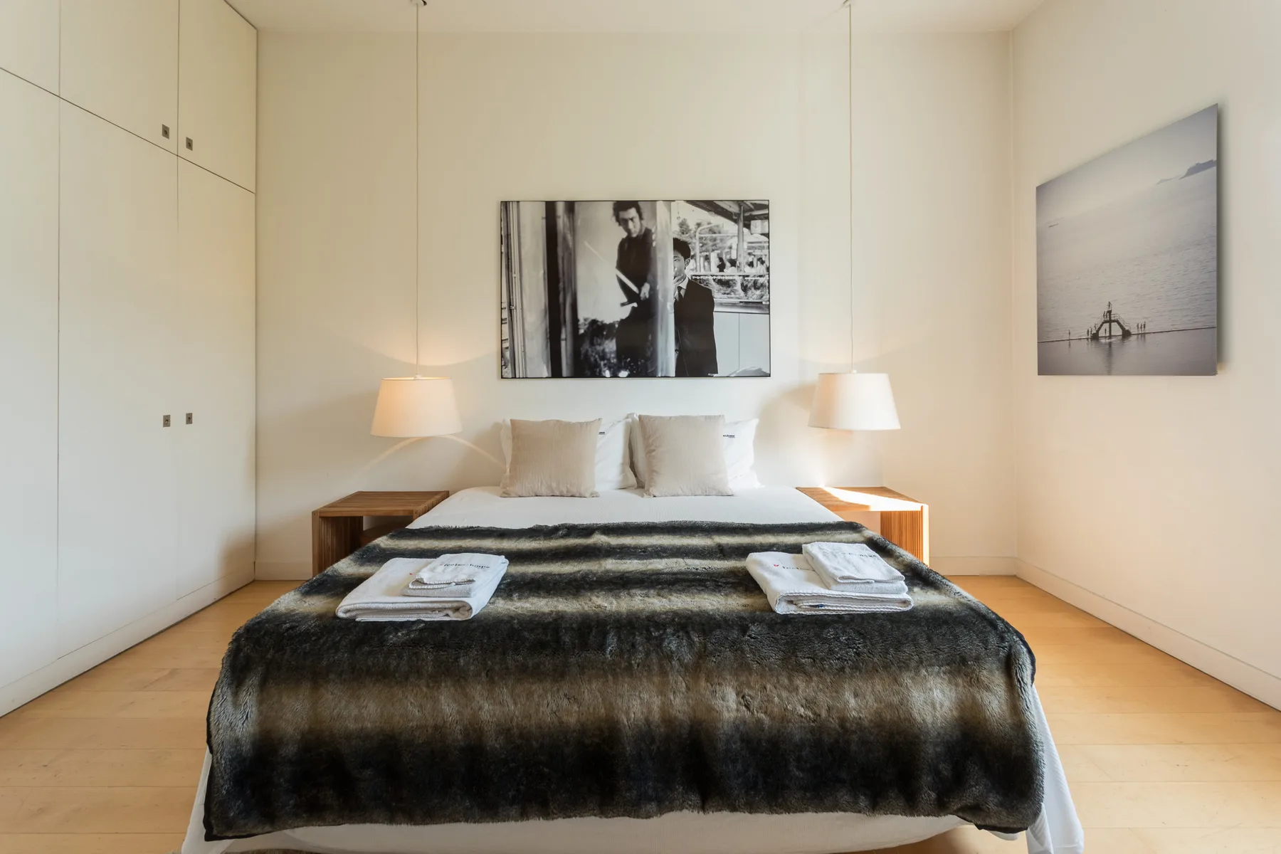 A bright bedroom with a neatly made bed and framed artwork on the walls.