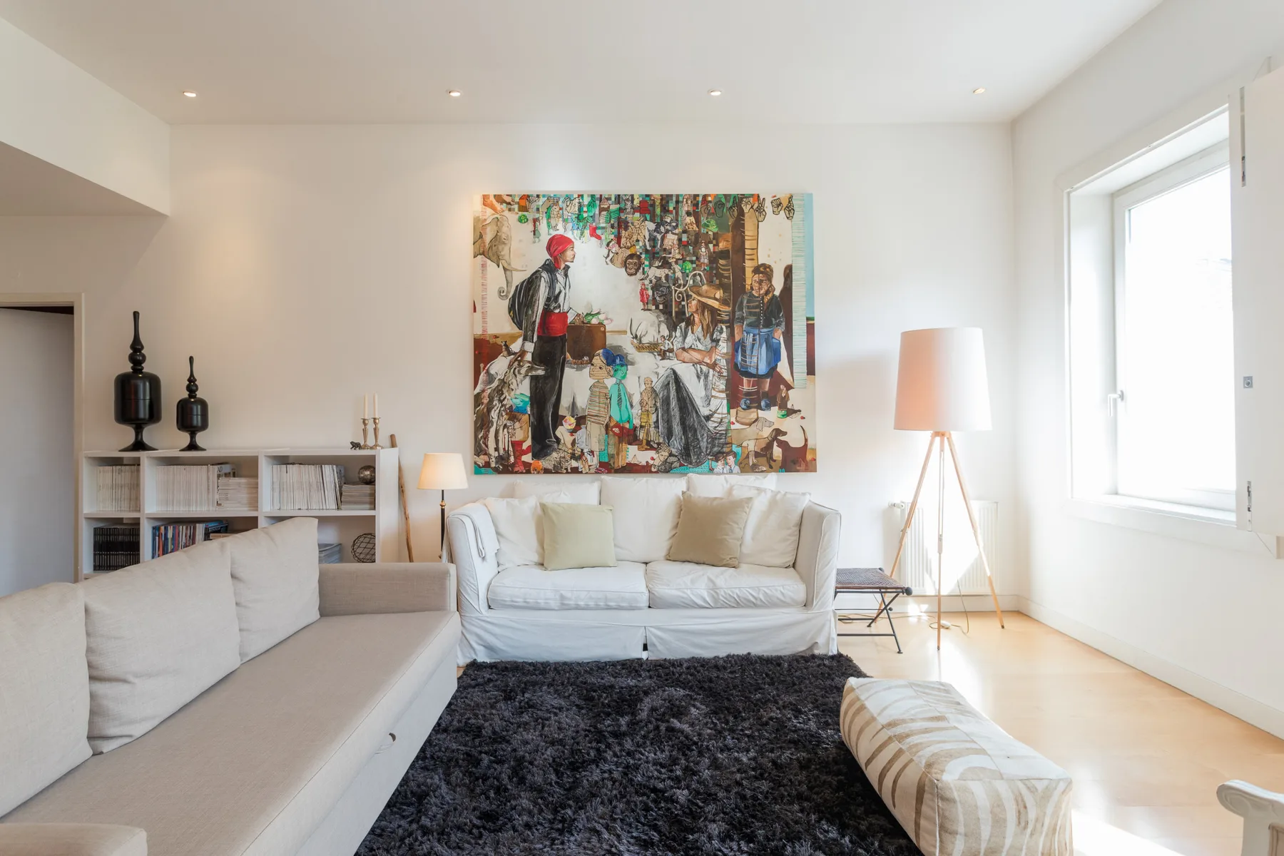 A bright living room with seating, a dark rug, and colorful wall art.