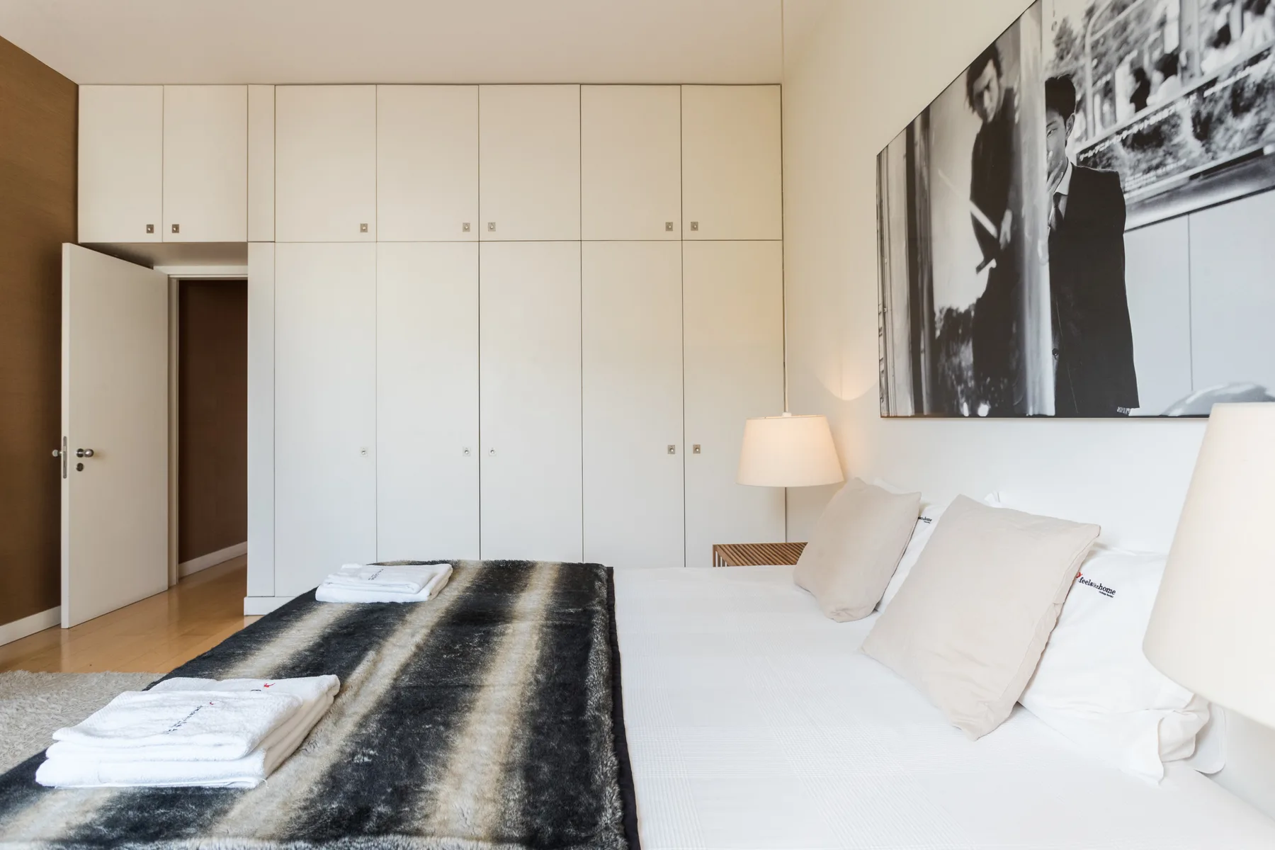 A bedroom with a white bed, patterned throw, and large wall artwork.