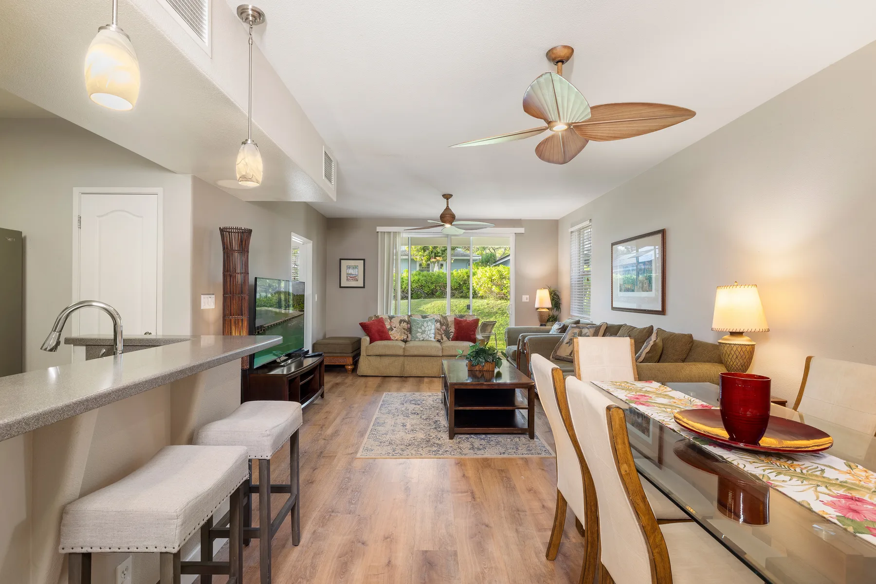 An open-plan living and dining area has a kitchen counter and windows overlooking greenery.