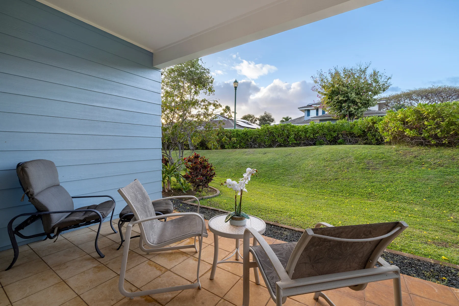 A covered patio with outdoor seating overlooks a green lawn and garden.
