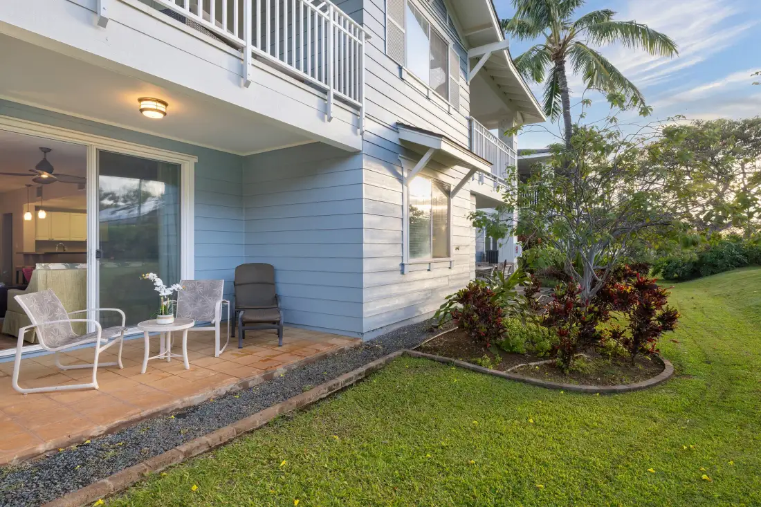 A blue-sided home has a covered patio with outdoor seating beside a landscaped lawn.