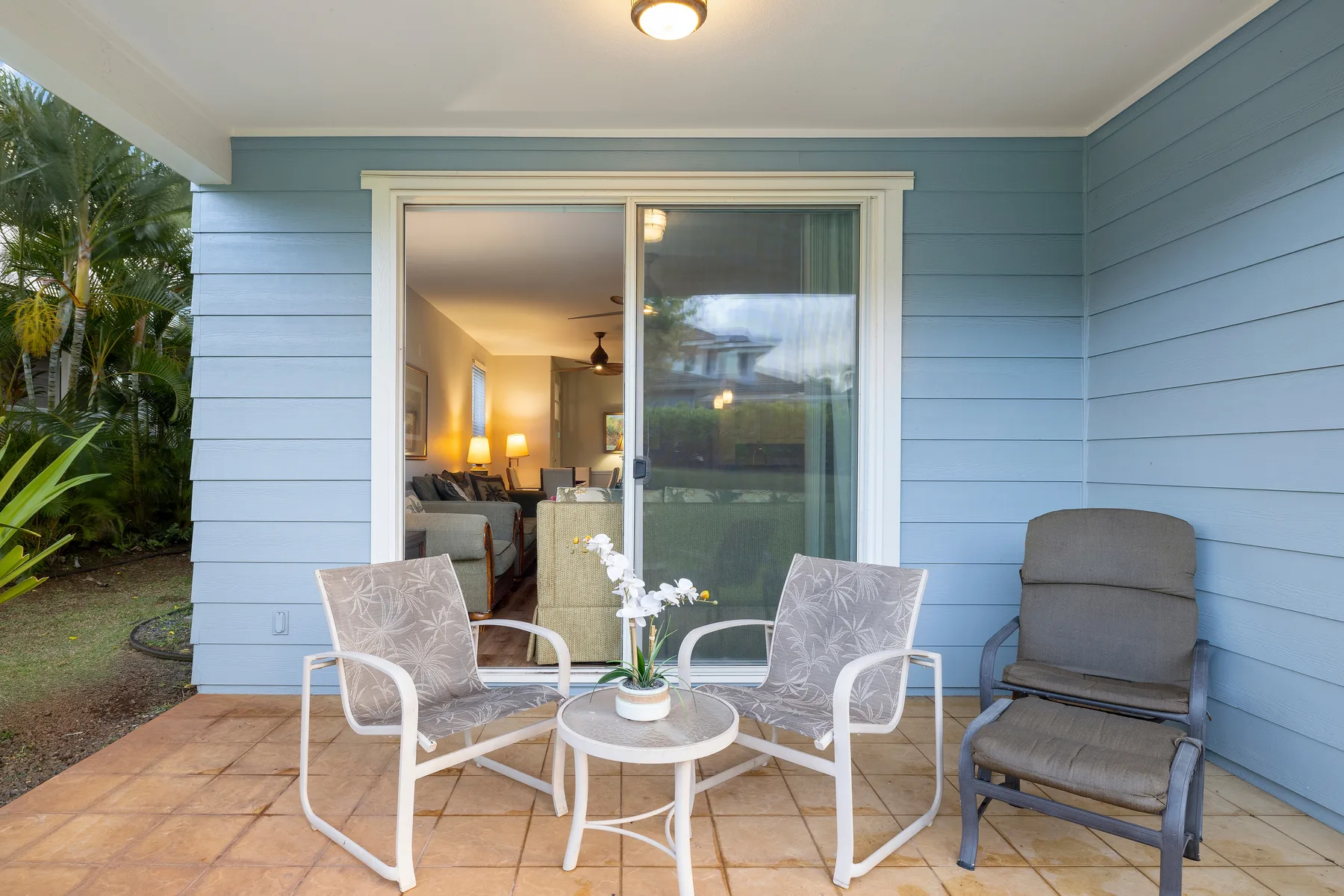 A covered patio with seating and a small round table sits beside a sliding glass door.